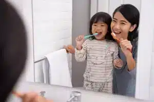 girl brushing teeth with mom